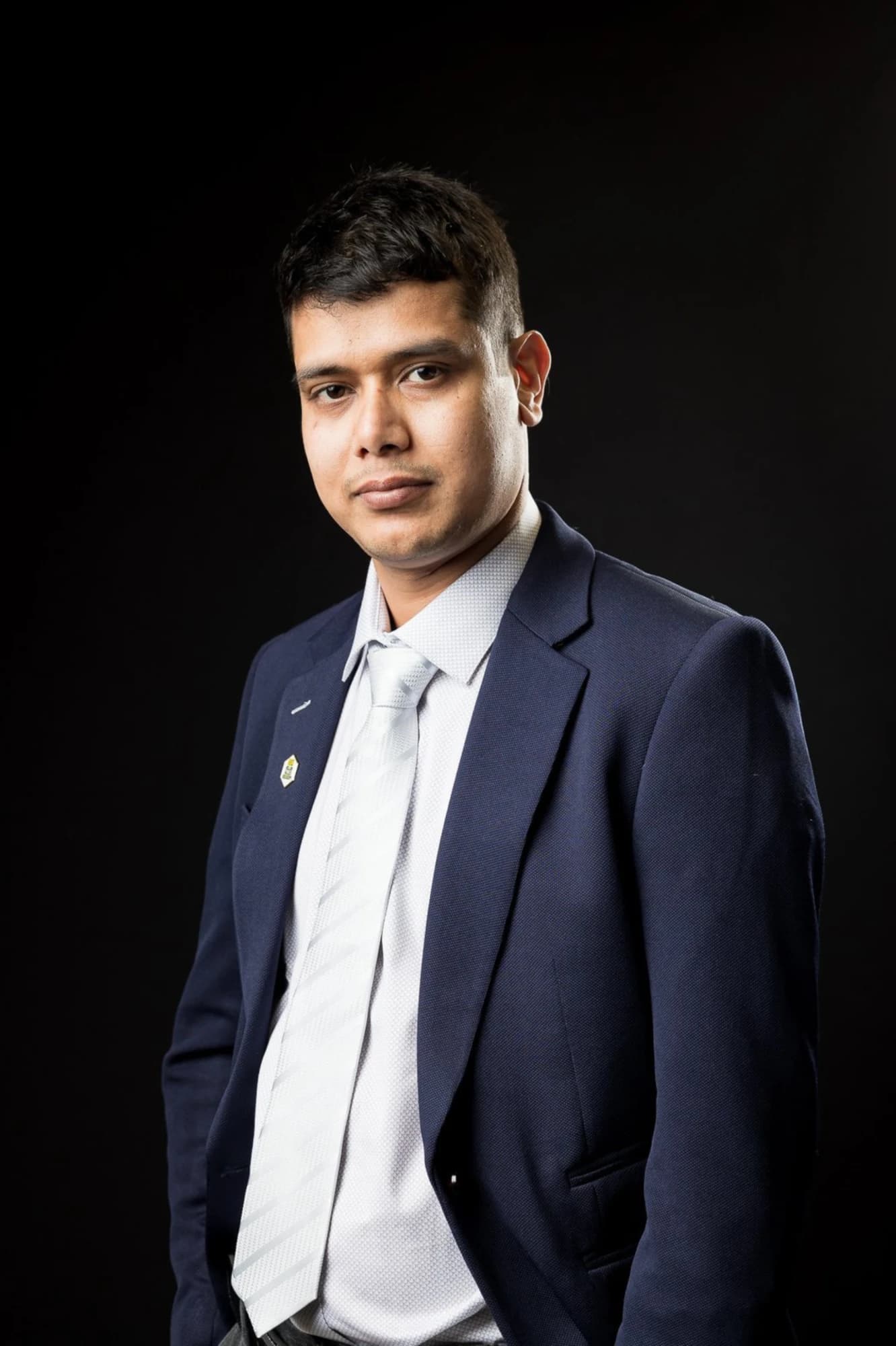 Khem Kadariya, founder of Living Rochester Suburbs, in a navy suit and silver tie against a black background