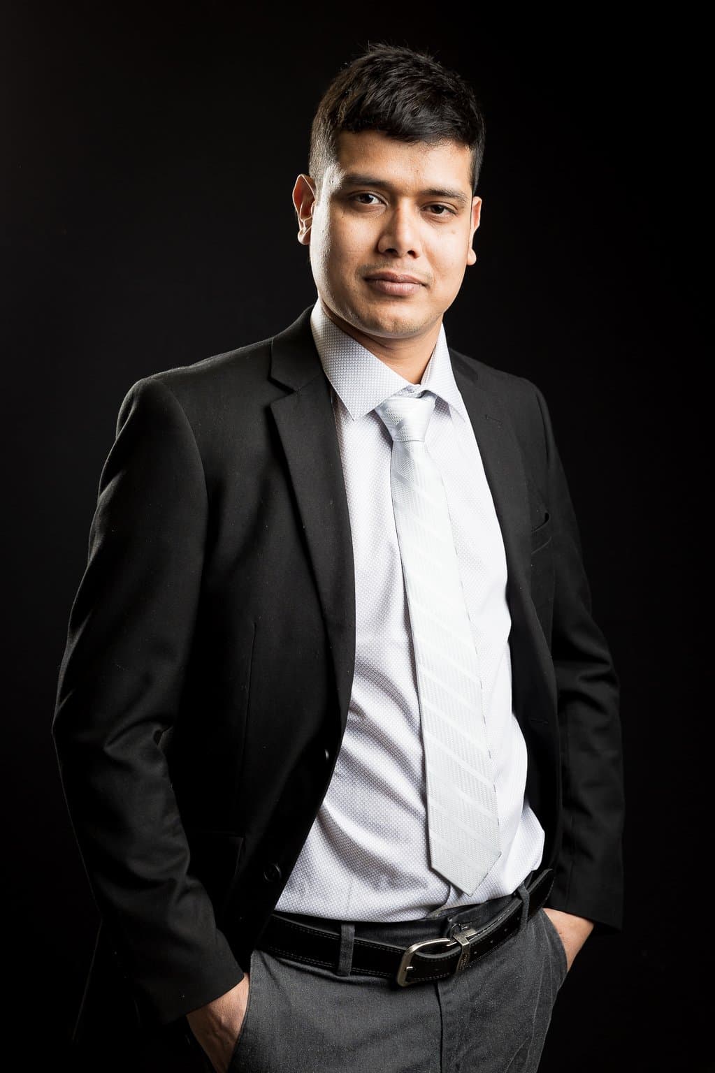 Khem Kadariya standing with hands in pockets against a dark background