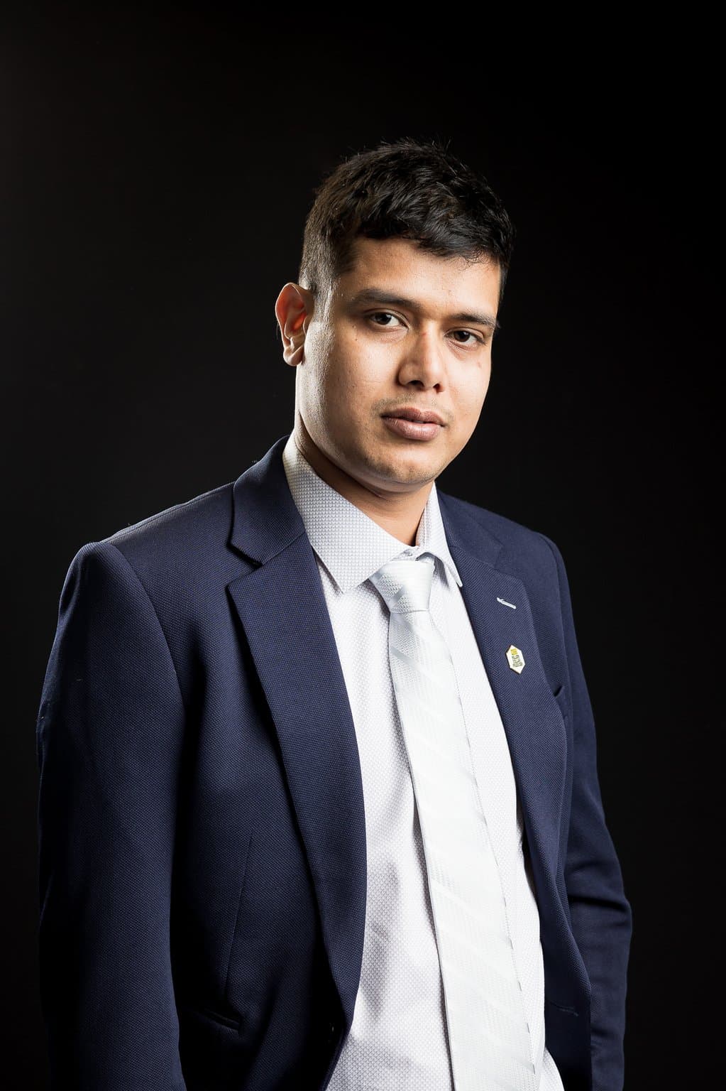 Khem Kadariya, founder of Living Rochester Suburbs, in a navy suit and silver tie against a black background